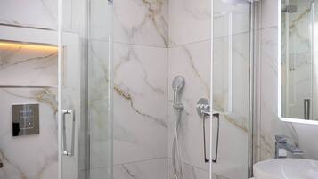 Une salle de bain moderne avec une douche à parois de verre, un lavabo blanc et un mur recouvert de carreaux de marbre.