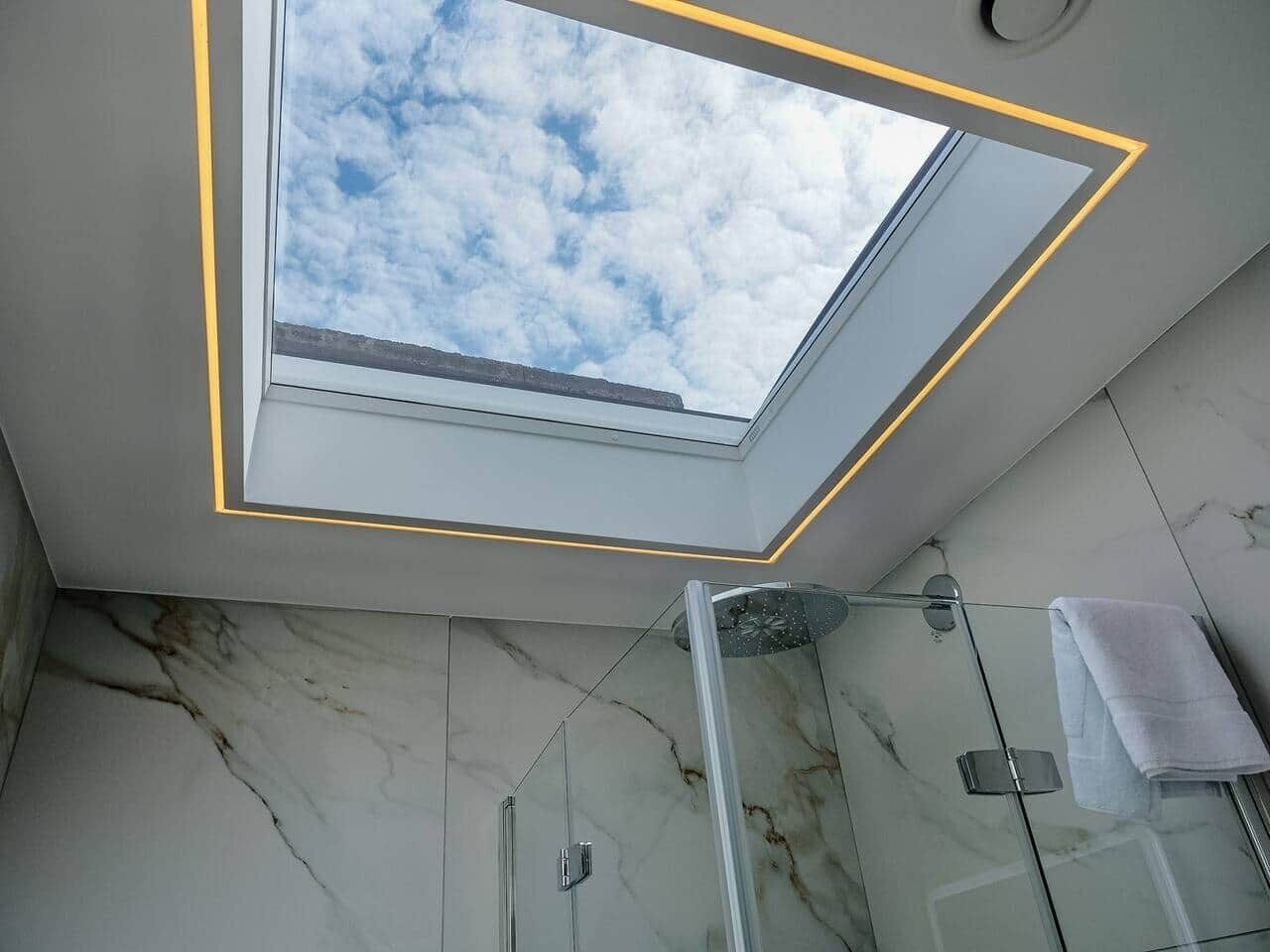 A skylight in a bathroom with marble walls and a glass shower enclosure.