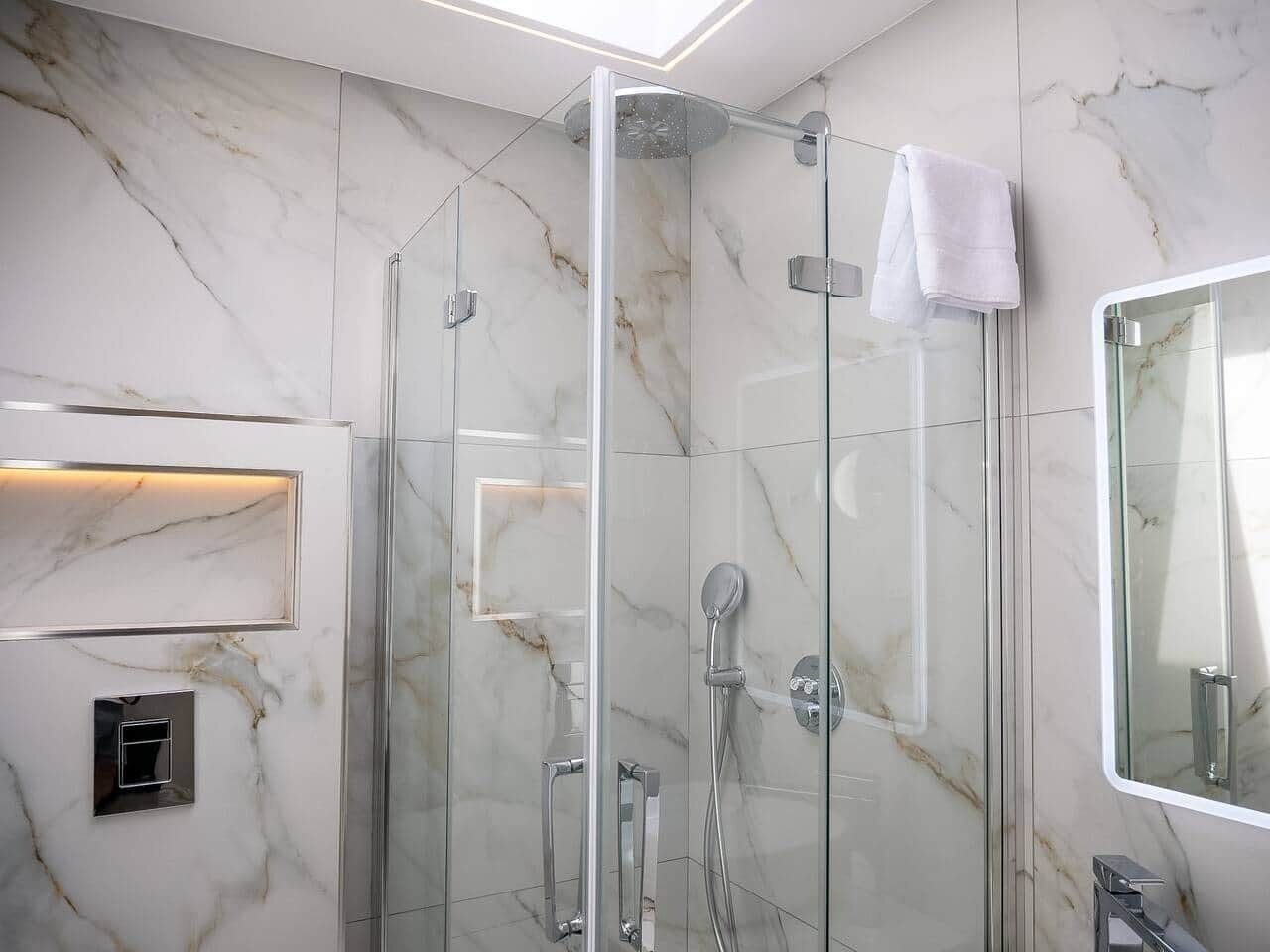 Un baño moderno con ducha envuelta en vidrio, un espejo grande y paredes de mármol.