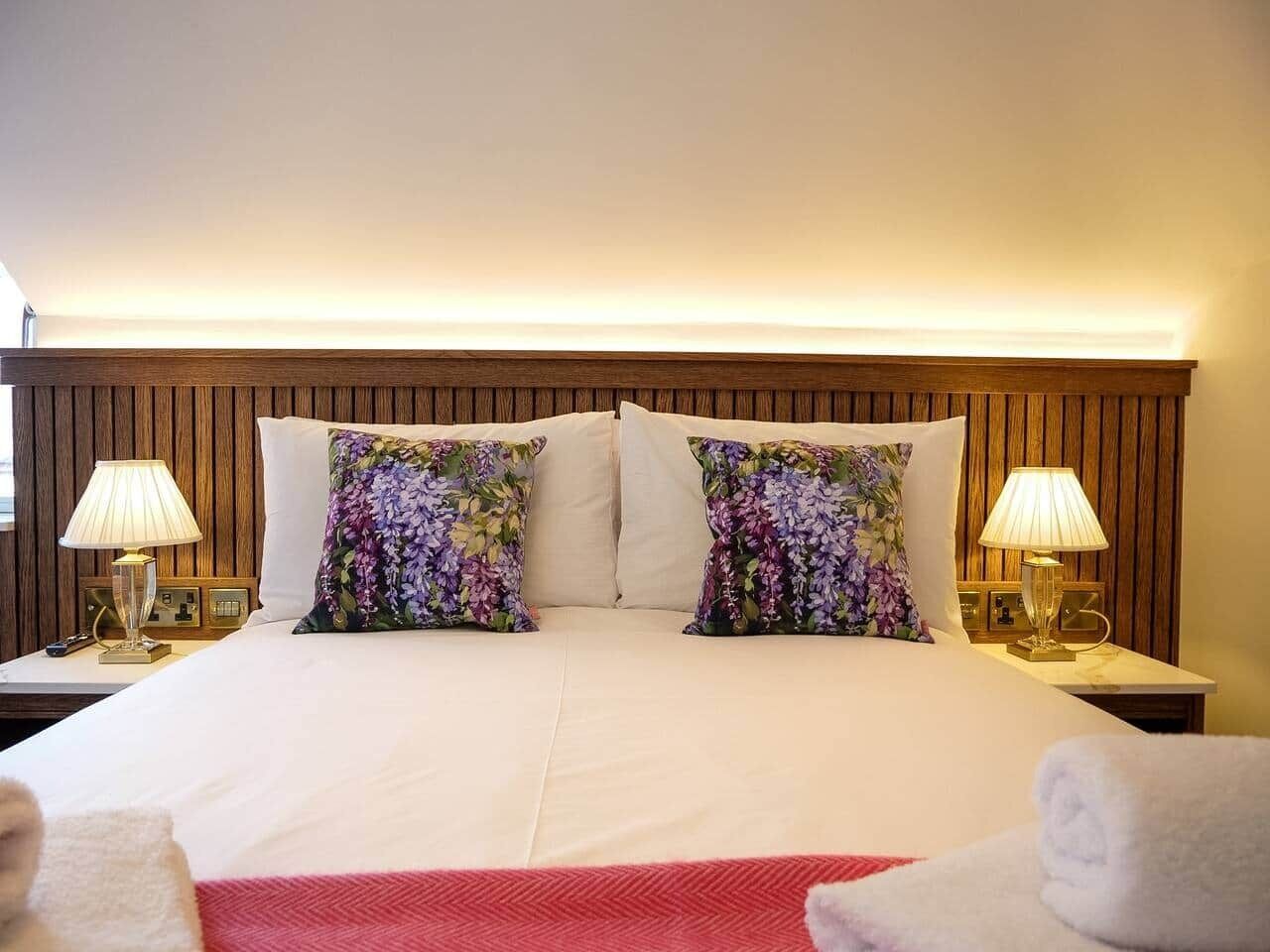 A hotel room with a large bed, two floral pillows, two bedside lamps, and a red throw blanket.