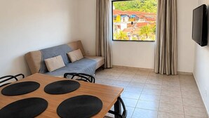 Une pièce avec une table en bois, des chaises noires, un canapé, un ventilateur de plafond, un téléviseur et une fenêtre avec des rideaux.