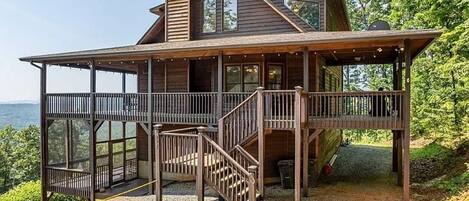 A wooden cabin with a covered porch, a staircase, and a view of the surrounding landscape.