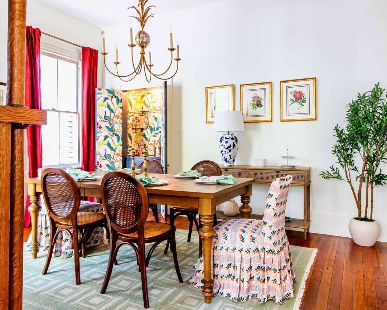 A dining area with a wooden table, wicker chairs, a chandelier, and a potted plant.