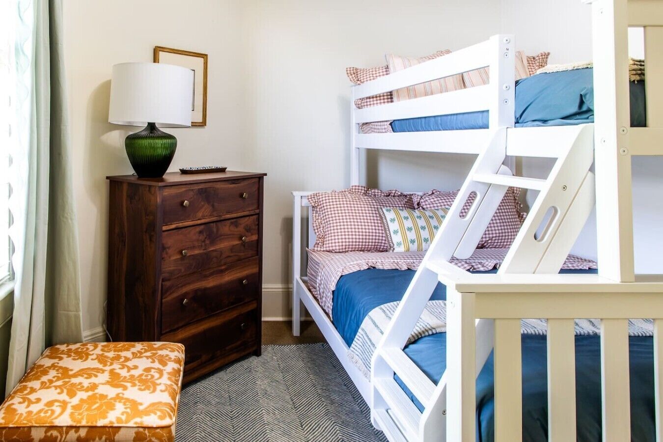 A child's bunk bed with a ladder, a wooden dresser, and a lamp.