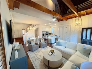 Un salon spacieux comprenant un canapé, des fauteuils, une table basse et un téléviseur. Un escalier mène à l’étage supérieur.