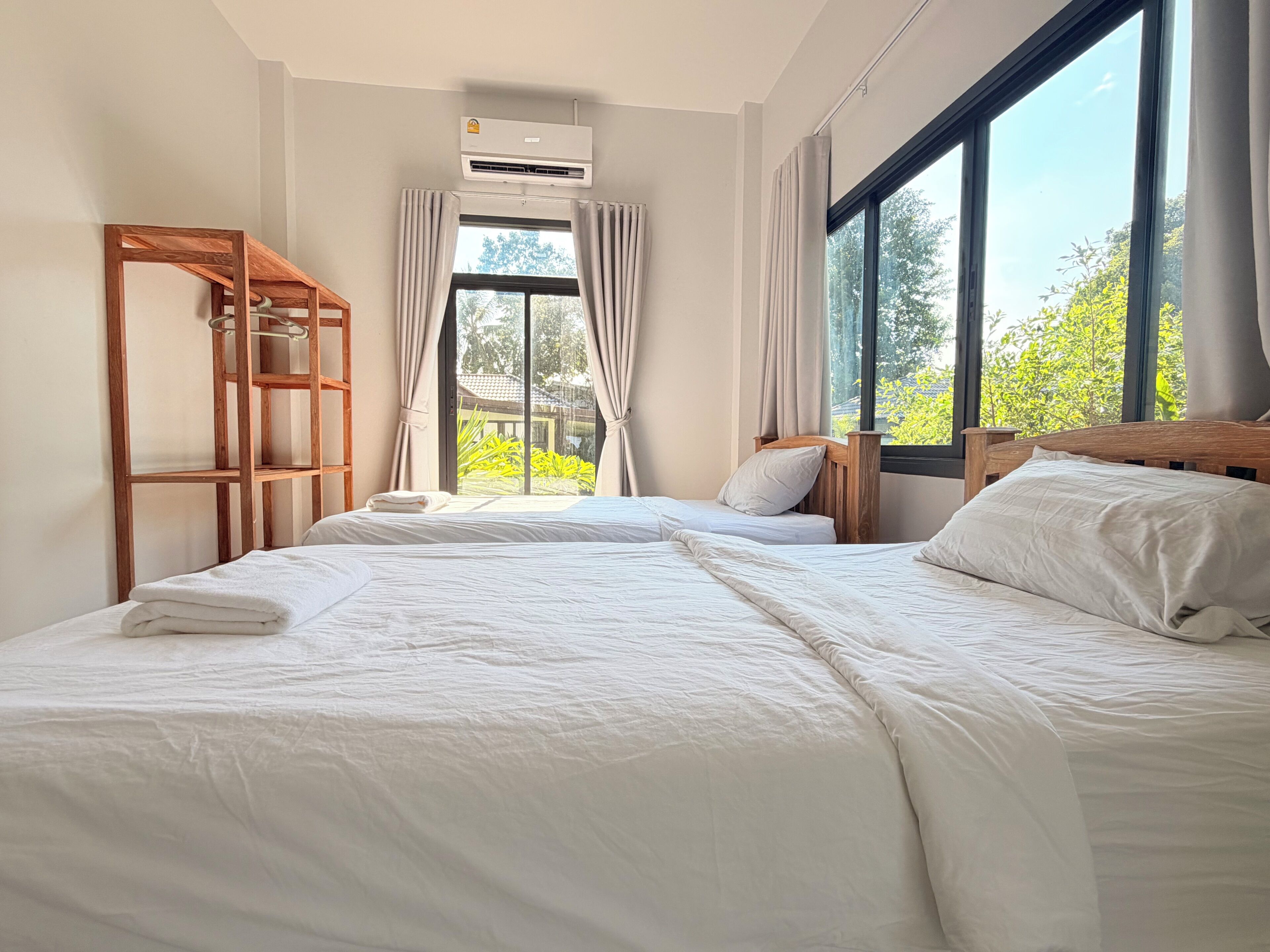 A hotel room with two beds, a wooden ladder, an air conditioning unit, and a large window with curtains.