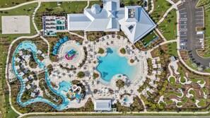 Vista aérea de un resort con una gran piscina, toboganes acuáticos y un edificio central con un diseño de techo distintivo.