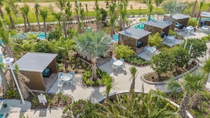 Eine Vogelperspektive zeigt ein Resort mit mehreren Poolbereichen, Sitzgelegenheiten im Freien und üppiger Bepflanzung.