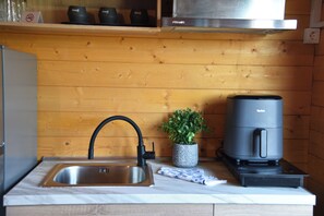 A kitchen with a stainless steel sink, a black faucet, a small potted plant, and a coffee machine.