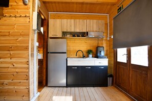 A compact kitchen with wooden walls, a refrigerator, a sink, and a stove.