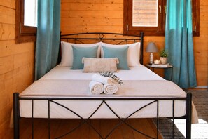 A wooden room with a bed, curtains, a bedside table with a lamp, and a small plant.