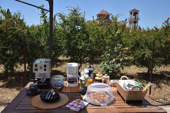Un coin pique-nique aménagé avec une machine à café, un panier et une table, le tout installé dans un vignoble avec un clocher en arrière-plan.