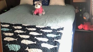 Un lit avec une couette, des oreillers, un jouet en peluche et un tableau accroché au-dessus.
