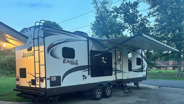 Un camping-car Jayco Eagle Premier est garé dans une allée, avec un espace de vie abrité et un petit garage attenant.