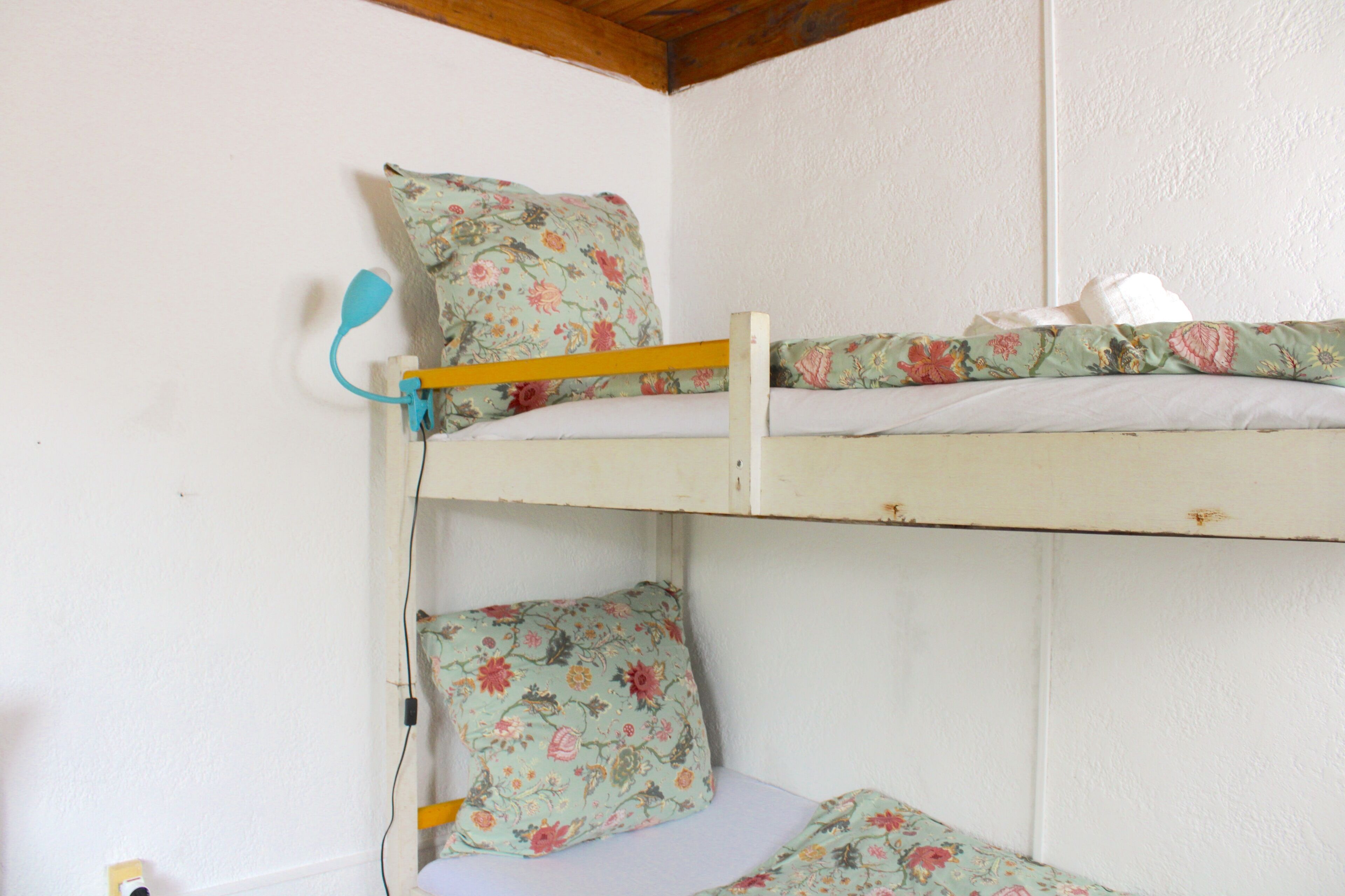 A bunk bed with floral bedding, a wooden headboard, and a white wall.