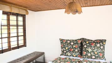 Une pièce avec un plafond en bois, un banc, un lit recouvert d’une literie à motifs floraux et un luminaire suspendu.