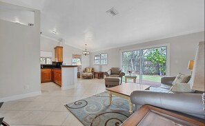 Ein geräumiges Wohnzimmer mit einer Couch, einem Couchtisch und Blick auf den Garten durch große Schiebeglastüren.