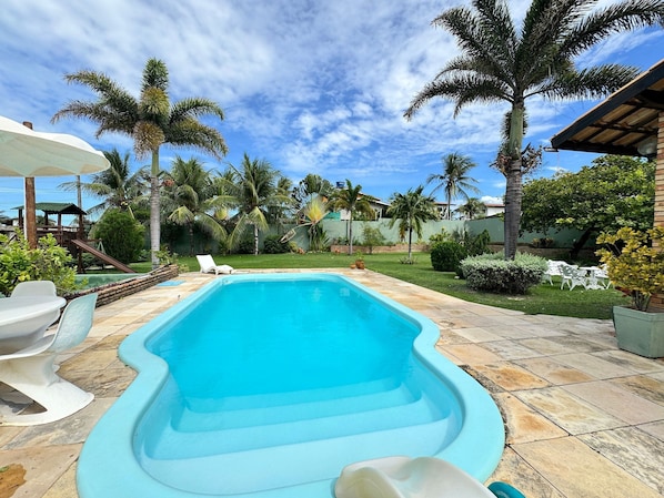 A swimming pool with a wavy edge, surrounded by palm trees and a grassy area. - Recanto Cajueiro (Aquiraz)