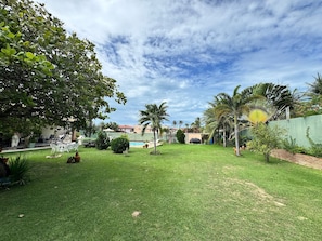 A well-maintained grassy yard with a pool, palm trees, and a brick wall. - Recanto Cajueiro (Aquiraz)