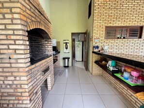 A kitchen with a brick oven, a refrigerator, and various kitchen items on the counter. - Recanto Cajueiro (Aquiraz)