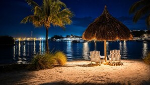 En strandscene med en stråtækt parasol, to stole og en palme.