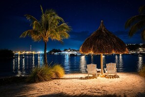 A beach scene with a thatched umbrella, two chairs, and a palm tree. - Sea View Apartment, Infinity Pool & Beach, 5 min Jan Thiel | B7 (Willemstad)