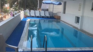 Une piscine avec une terrasse bleue, des chaises longues blanches et un parasol bleu.