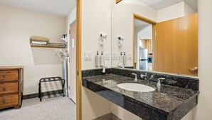 Une salle de bain avec un lavabo en marbre noir, deux miroirs, un porte-serviettes et un petit tabouret noir.