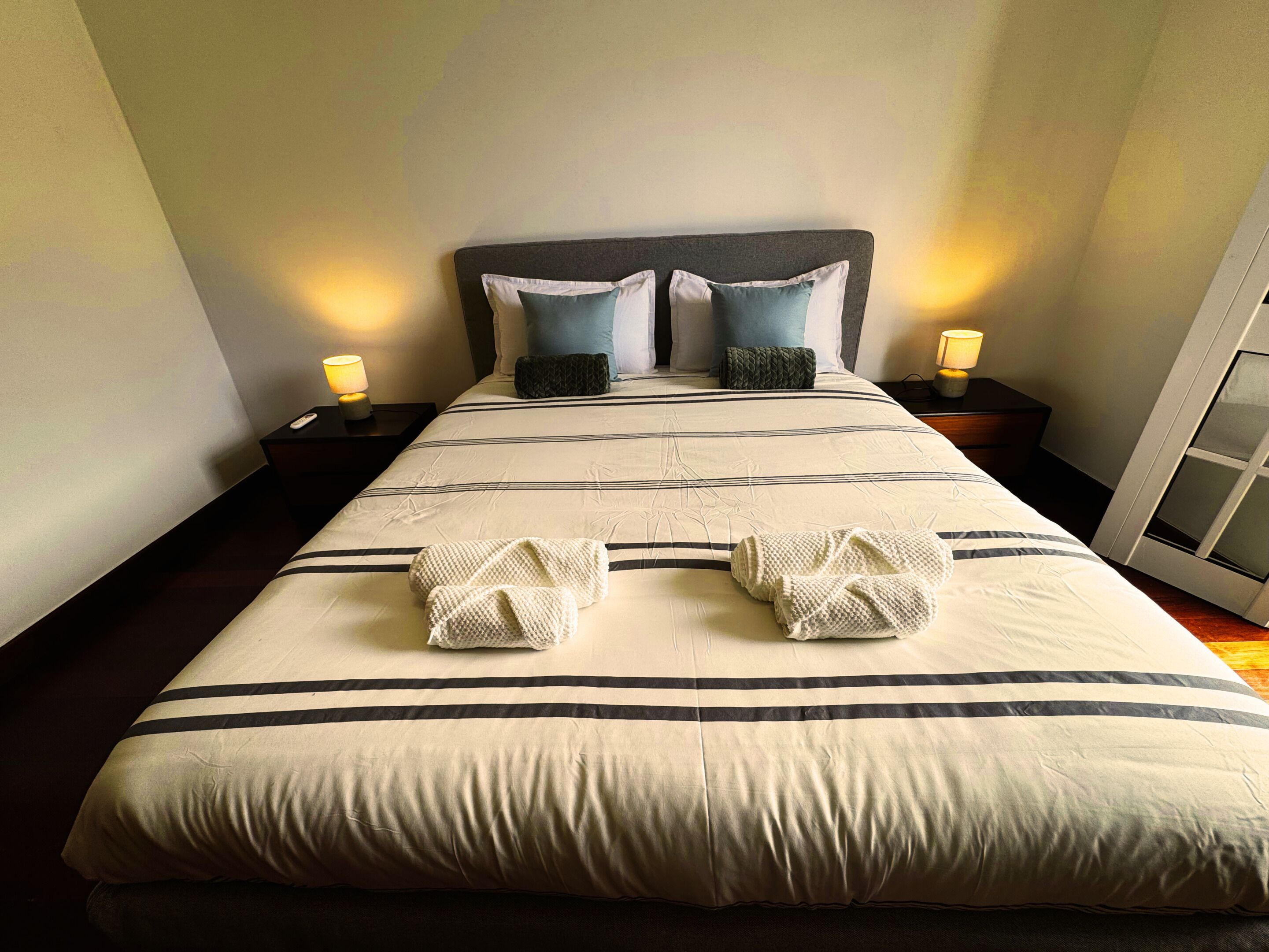 Una cama bien hecha con un edredón a rayas, dos almohadas y dos lámparas de noche.
