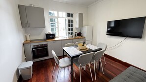 Eine kleine Küche mit Mikrowelle, Toaster und Spüle. Ein Esstisch mit Stühlen und ein an der Wand befestigter Fernseher.