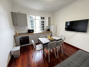 A compact kitchen with a microwave, toaster, and sink. There is a dining table with chairs and a television mounted on the wall.
