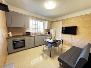 A compact kitchen with a dining area, a sofa, and a TV mounted on the wall.