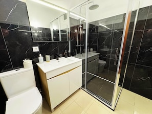 A modern bathroom with a glass shower enclosure, a white sink, and a toilet. - Wolf Villa (Câmara de Lobos)