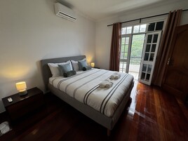 A bedroom with a bed, bedside tables, an air conditioning unit, a window with curtains, and a door.