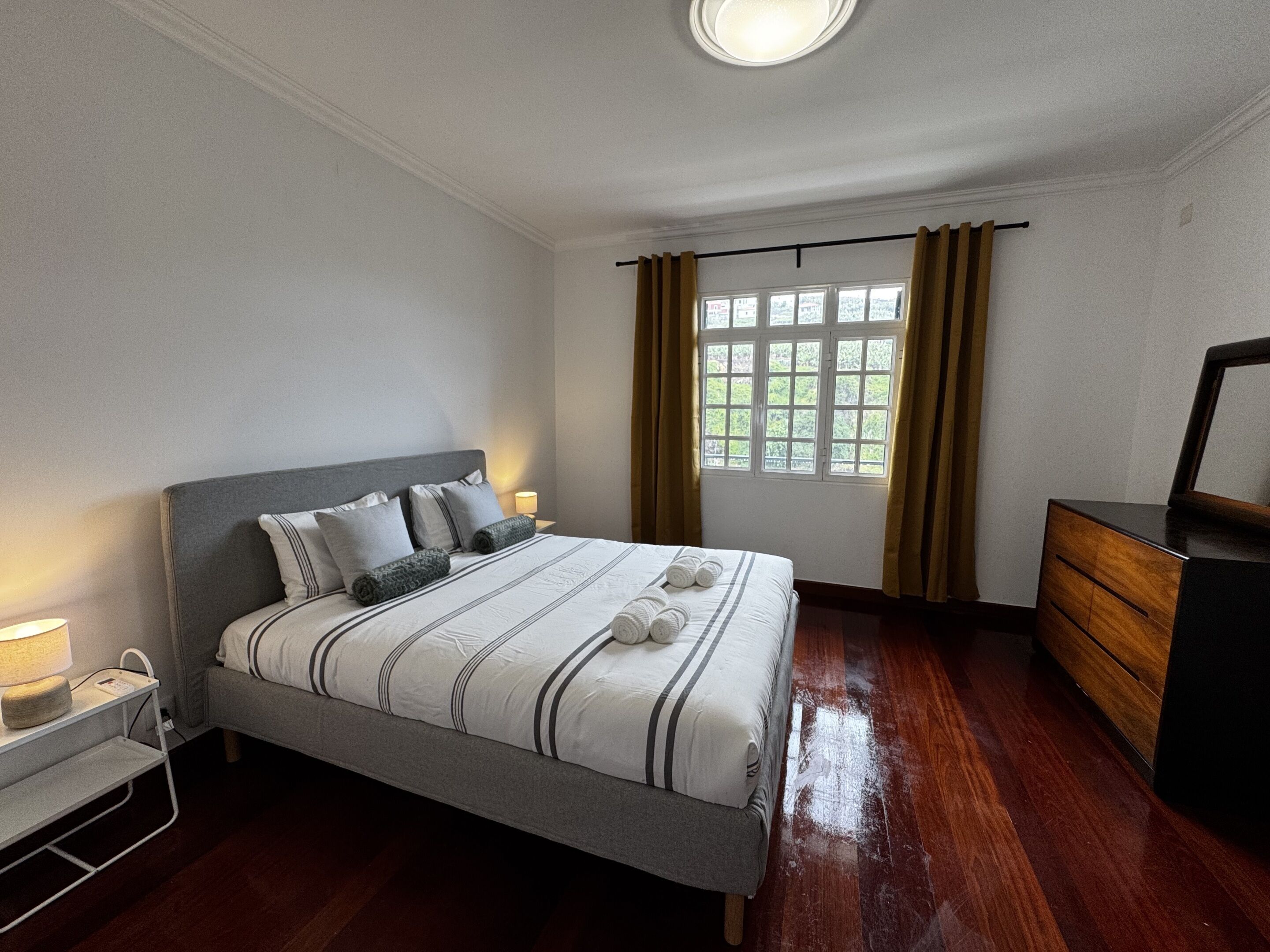 A neatly arranged bedroom with a bed, bedside lamps, a dresser, and a window with curtains.