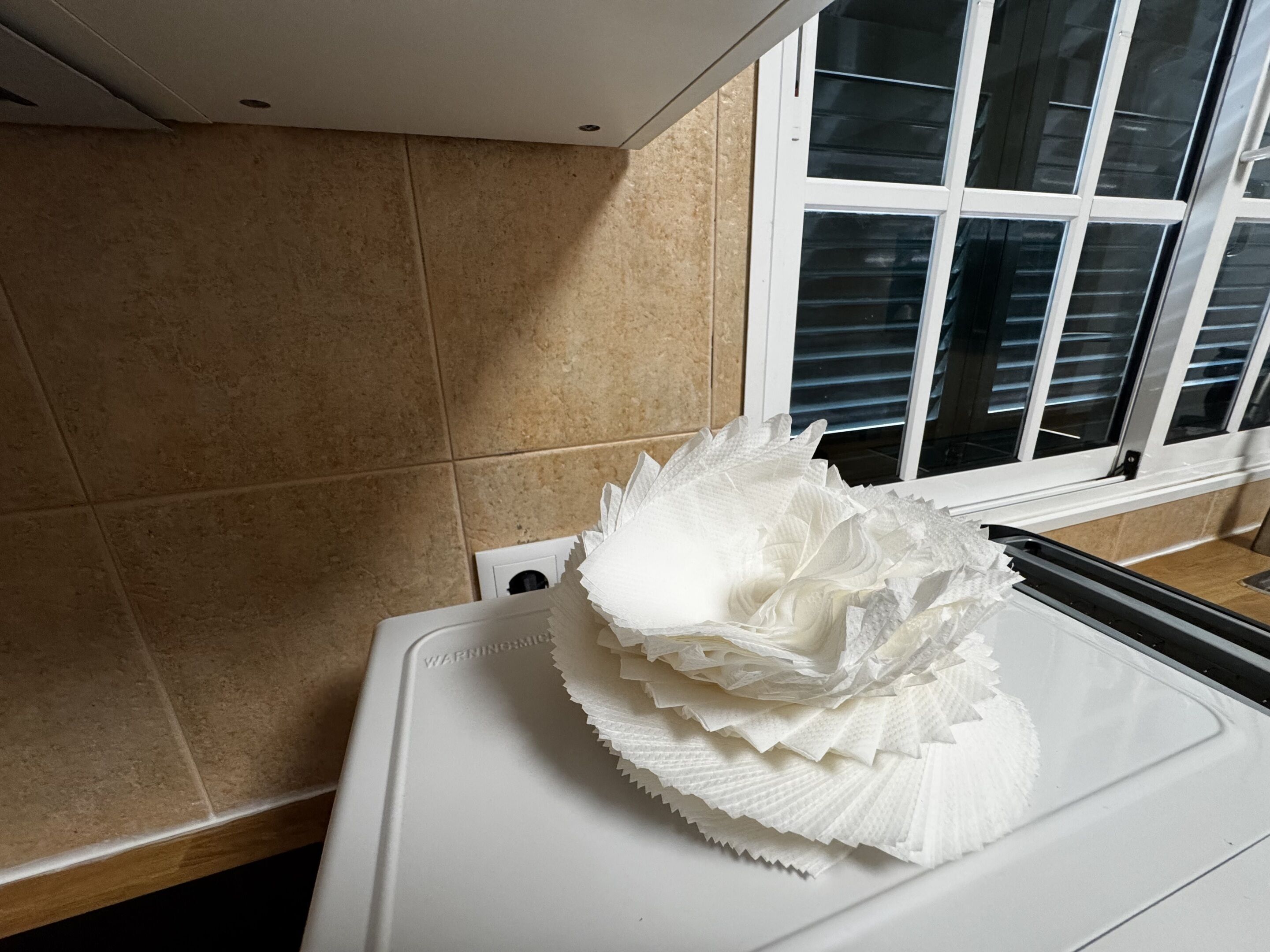 A kitchen counter with a white appliance and a window with blinds.