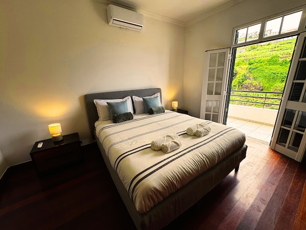 A bedroom with a bed, bedside lamps, an air conditioner, and a view through a glass door. - Wolf Villa (Câmara de Lobos)