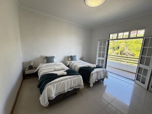 A bedroom with two beds, a nightstand, a lamp, and a sliding glass door leading to a balcony. - Wolf Villa (Câmara de Lobos)