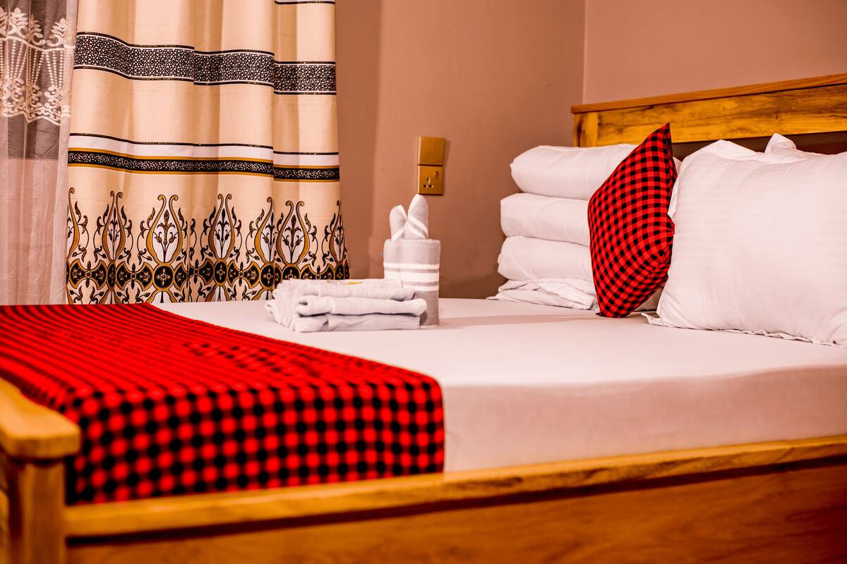 A neatly made bed with white linens, a red and black checkered blanket, and a red checkered pillow.
