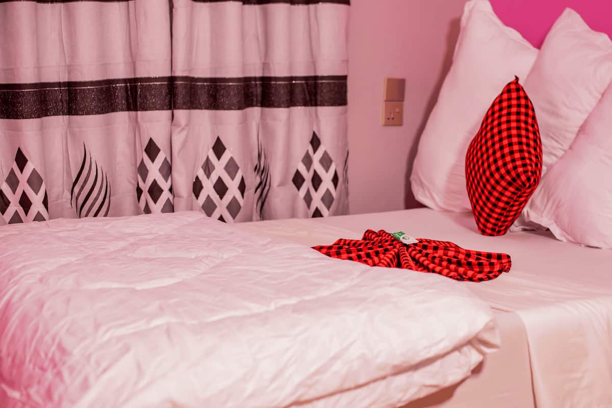 A bed with a white bedspread, a red and black checkered blanket, and a pillow with a similar pattern.