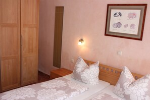 Ein Schlafzimmer mit Bett, Kissen, einem Nachttisch, einem gerahmten Bild an der Wand und einem Holzschrank.