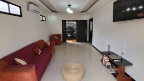 A living room with a red sofa, a woven floor mat, a bookshelf, and a TV on the wall. - Congo House. Cottage in Golfito (Golfito)