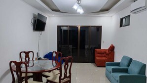 A living room with a glass-top dining table, wooden chairs, a red sofa, a blue sofa, a TV mounted on the wall, and a sliding glass door leading to another room. - Congo House. Cottage in Golfito (Golfito)