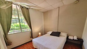 A room with a bed, a nightstand, a window with curtains, and a patterned floor. - Congo House. Cottage in Golfito (Golfito)