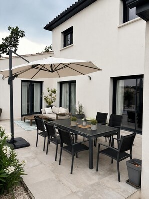 Eine Terrasse im Freien mit Esstisch, Stühlen, Sonnenschirm und einer Couch.