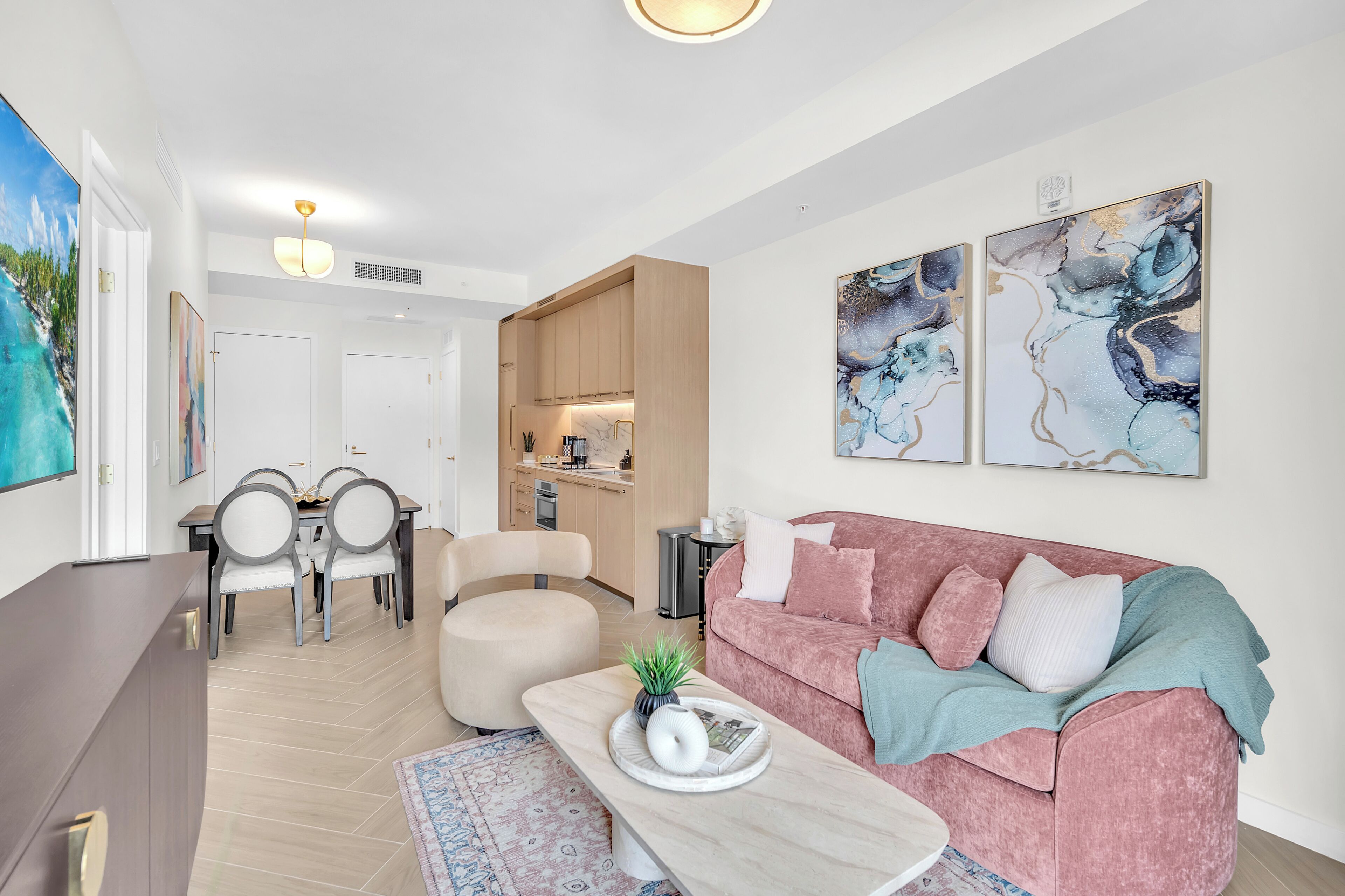 Una sala moderna con un sofá rosa, una zona de comedor con mesa y sillas, y una cocina al fondo.