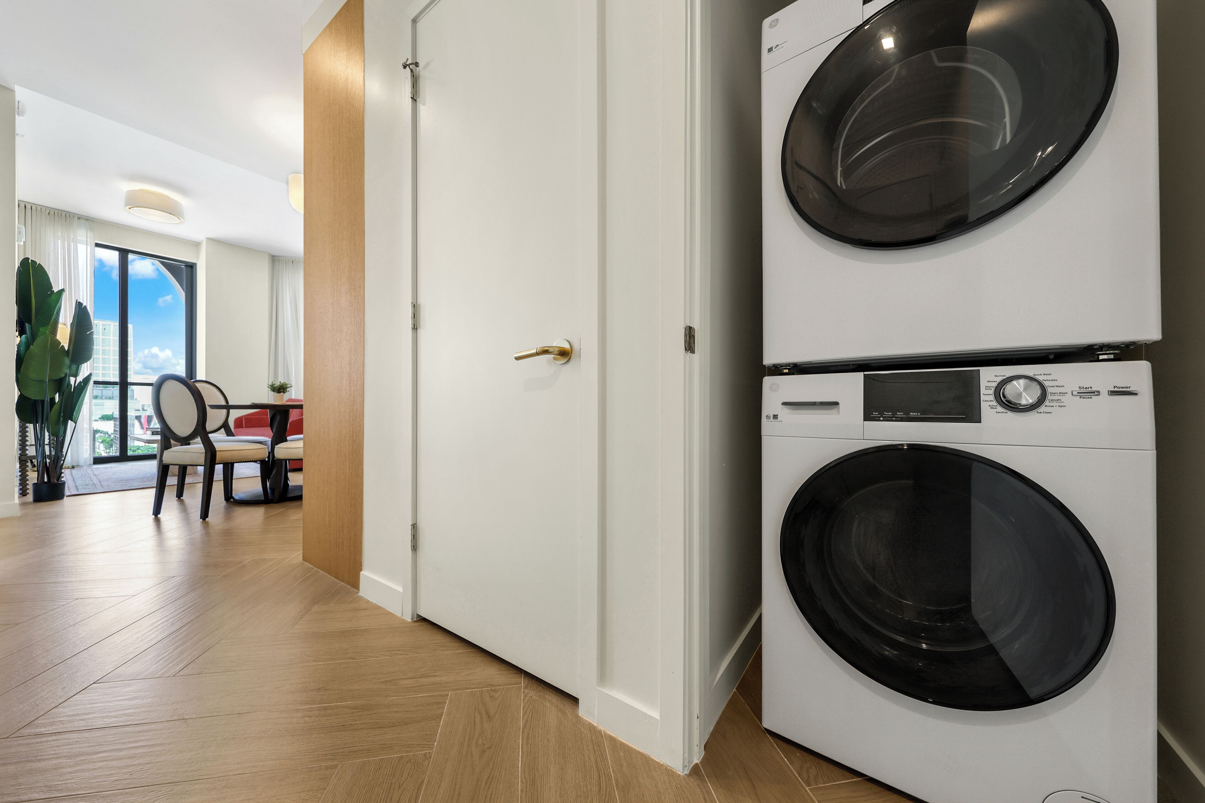 Un lavadero con dos lavadoras apiladas, una puerta y una zona de comedor con sillas y una mesa.
