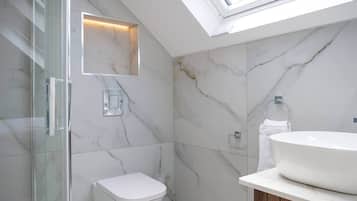 A modern bathroom with a skylight, a glass shower enclosure, a toilet, and a sink with a wooden vanity.