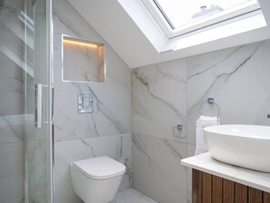 Un baño moderno con tragaluz, cabina de ducha de vidrio, inodoro y lavamanos con tocador de madera.