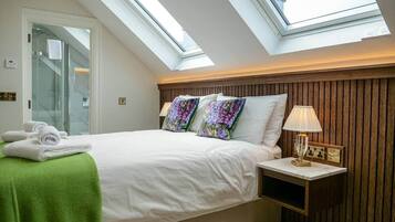 A bedroom with a skylight, a bed with white bedding, a green throw, and a nightstand with a lamp.
